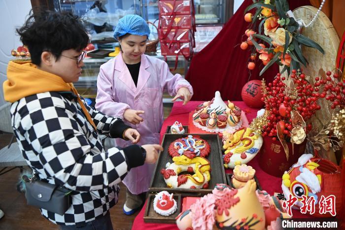 1月25日，隨著春節(jié)臨近，蘭州一花饃店“龍”元素花饃熱銷。圖為工作人員向顧客推薦“龍”元素花饃。九美旦增 攝</p><p>